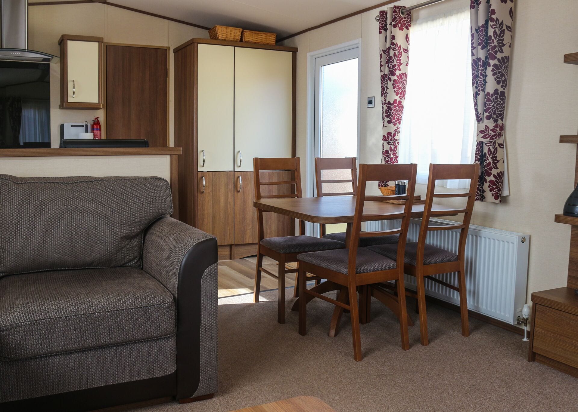 Een kleine woonruimte met een bank, een eettafel, stoelen, een kitchenette en een garderobe.