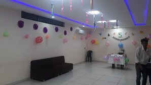 Une pièce avec un plafond blanc, plusieurs luminaires encastrés, un canapé marron foncé, une table recouverte d’une nappe blanche et des ballons accrochés aux murs.