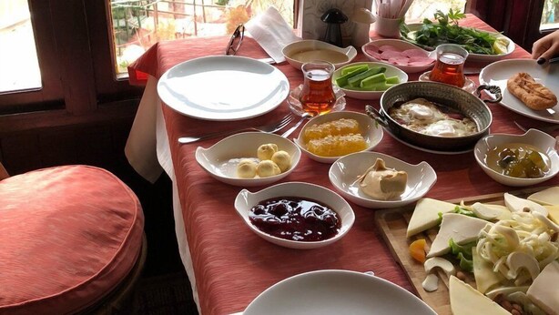 Une table à manger dressée avec différents plats, et une vue sur une forêt par de grandes fenêtres.