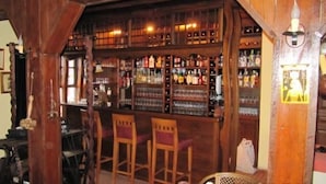 Un bar avec des étagères en bois remplies de bouteilles, deux tabourets de bar en bois et un luminaire suspendu.