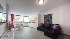 A modern living area with a black sofa, a dining table, and a kitchen in the background. - Charming apartment with swimming pool 5 min from the sea  (San Bartolomé de Tirajana)