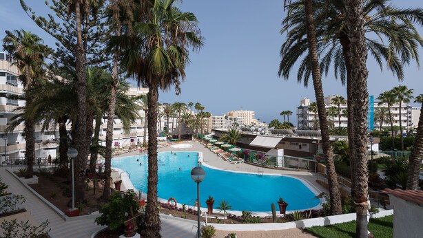A large outdoor swimming pool surrounded by palm trees and a hotel building in the background. - Charming apartment with swimming pool 5 min from the sea  (San Bartolomé de Tirajana)