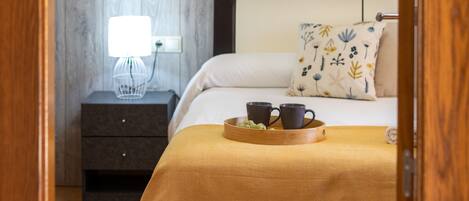 Un dormitorio con cama, mesita de noche, lámpara y un cuadro en la pared.