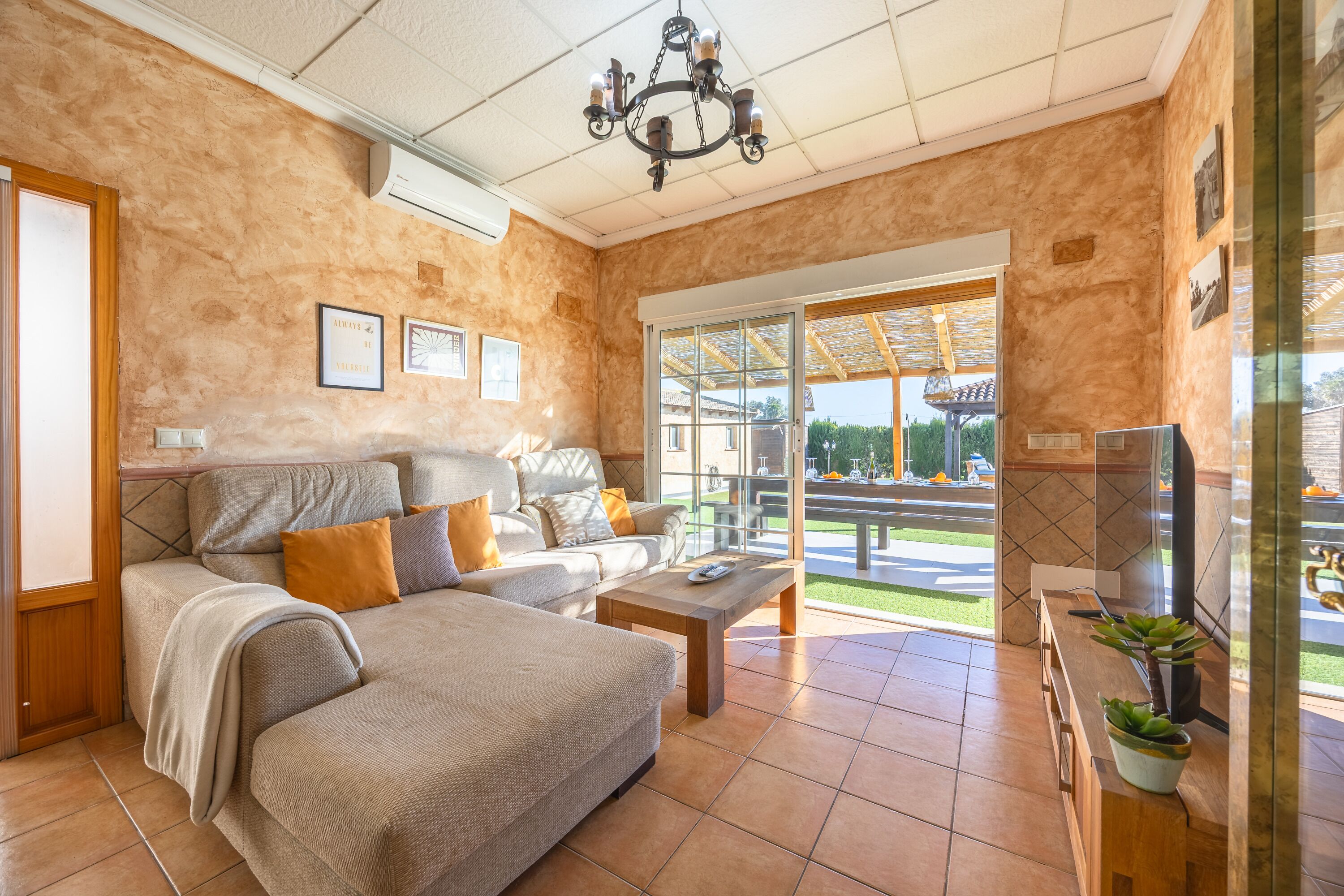 Ein geräumiges Wohnzimmer mit einer Couch, einem Couchtisch und einem Fernseher. Ein großes Fenster bietet einen Blick ins Freie.