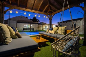 Un espace extérieur aménagé avec des sièges, une piscine, des meubles en bois et des guirlandes lumineuses.