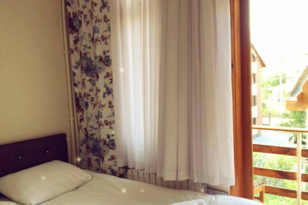 A bedroom with a bed, curtains, and a window with a view of a wooden deck.