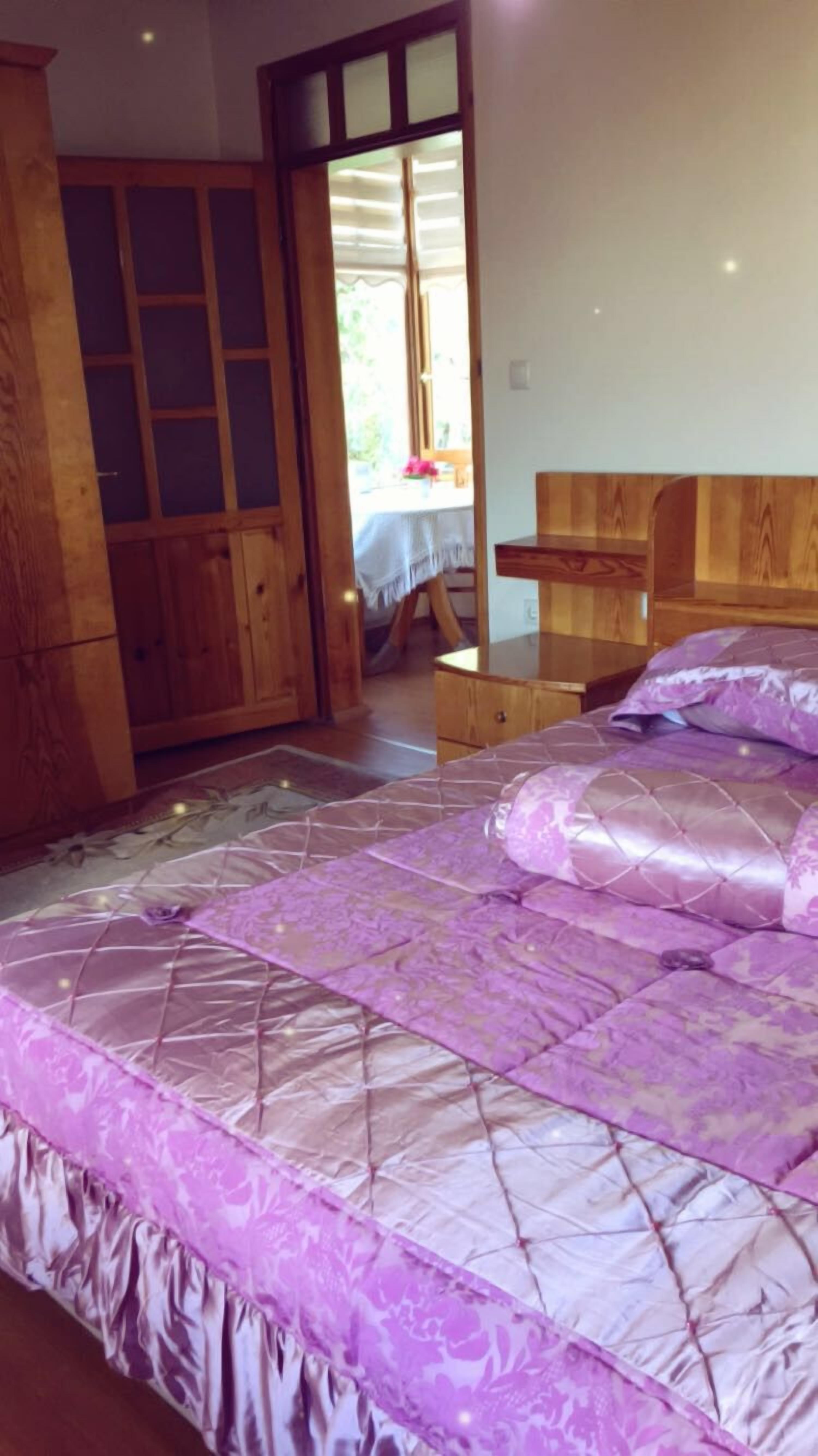 A bedroom with a large bed, wooden wardrobe, and a window with blinds.