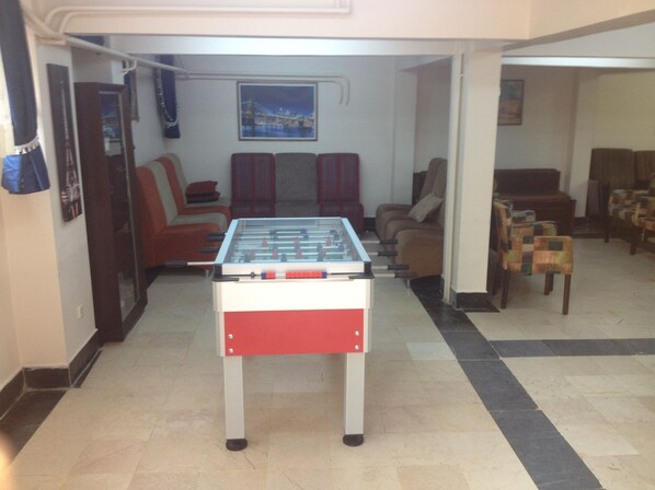 Una habitación con mesa de fútbol de mesa, sillas marrones y rojas, un sofá y un cuadro en la pared.