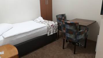 Un dormitorio pequeño con una cama individual, un escritorio de madera, dos sillas y un armario.