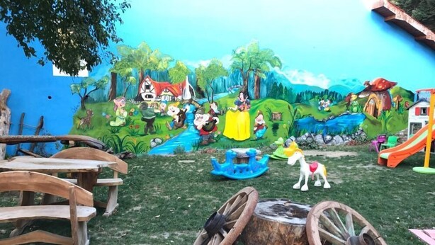 A children's play area with a mural, wooden play structures, and a slide. - Bolu Yildiz Hotel (Bolu)