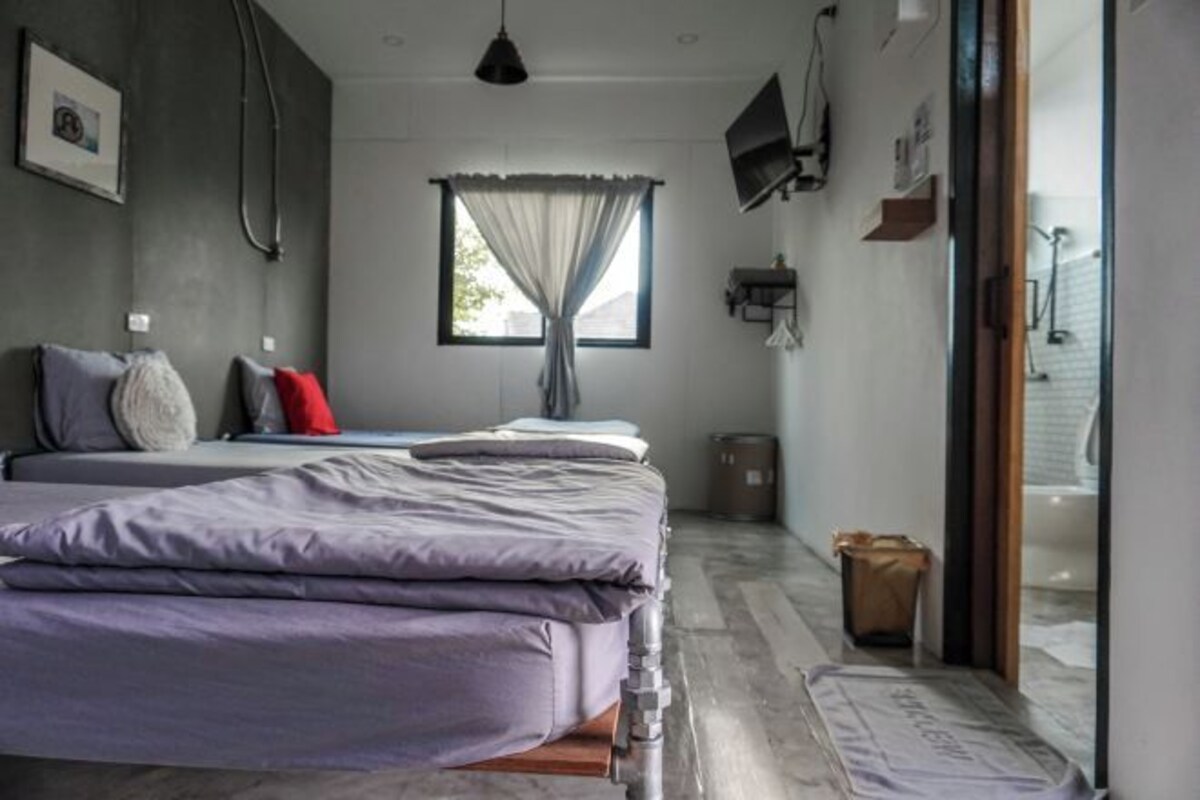 A bedroom with a bed, a window with curtains, a television on the wall, and a door leading to another room.