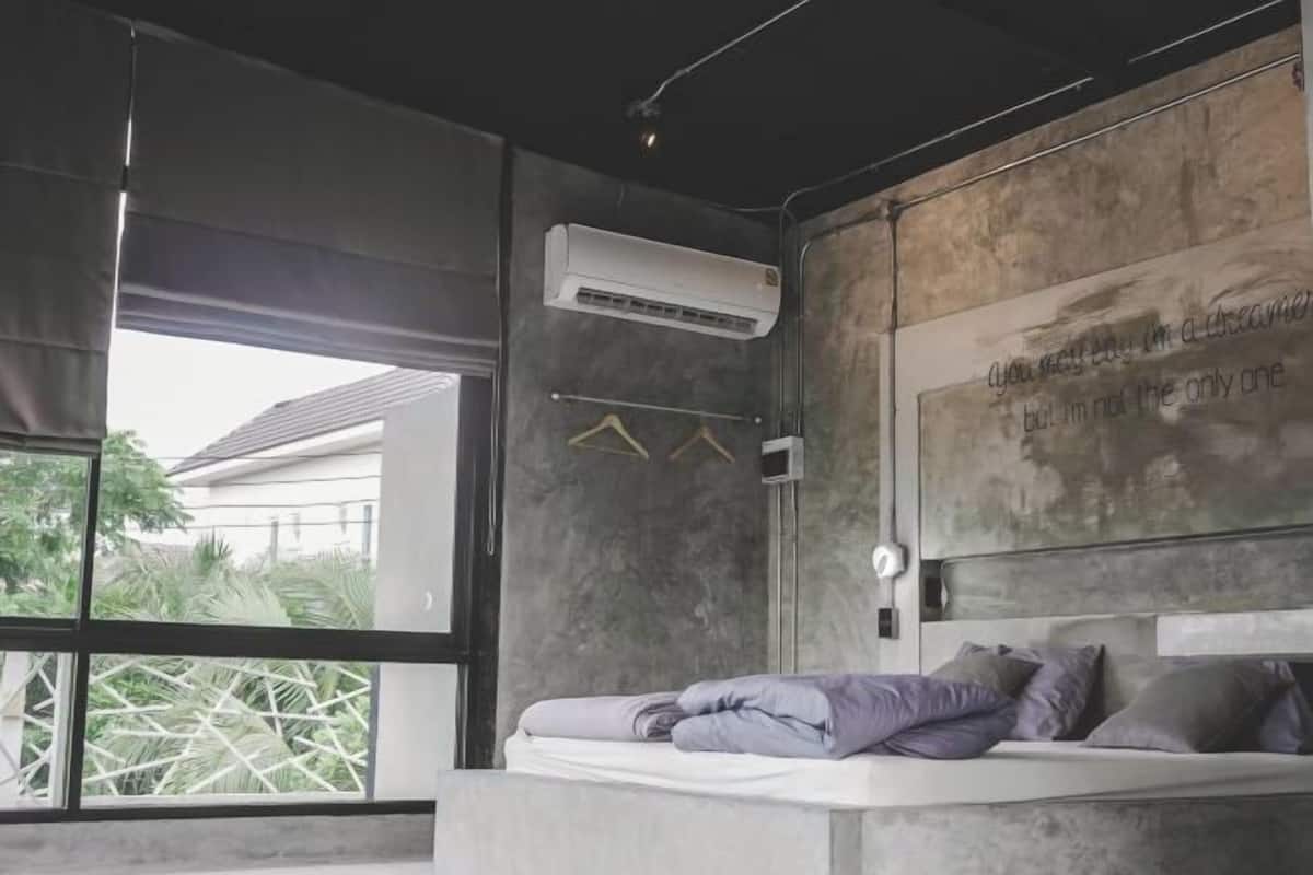 A modern bedroom with a large window, a bed with pillows, a wall-mounted air conditioner, and a wall with text.