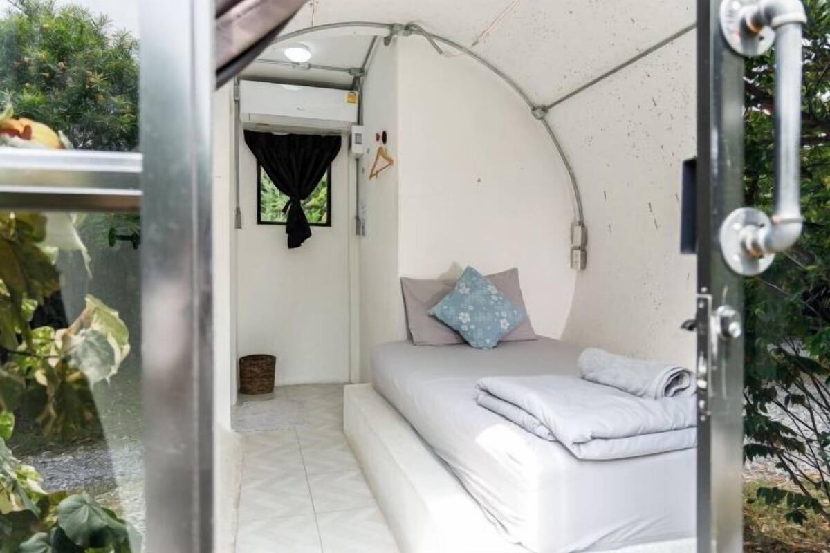 A compact, well-lit room with a bed, a small window with curtains, and a door.