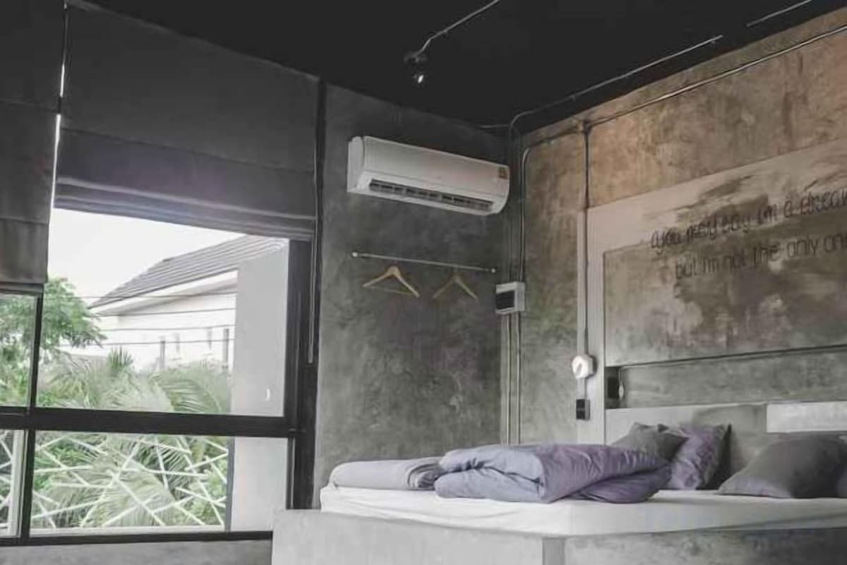 A modern bedroom with a concrete bed, a wall-mounted air conditioner, and a view through a large window.