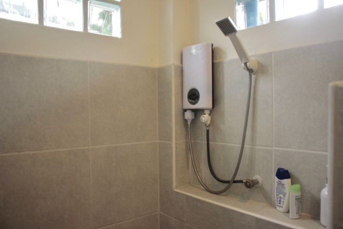 A shower area with a handheld showerhead, a wall-mounted control unit, and toiletries on a shelf.