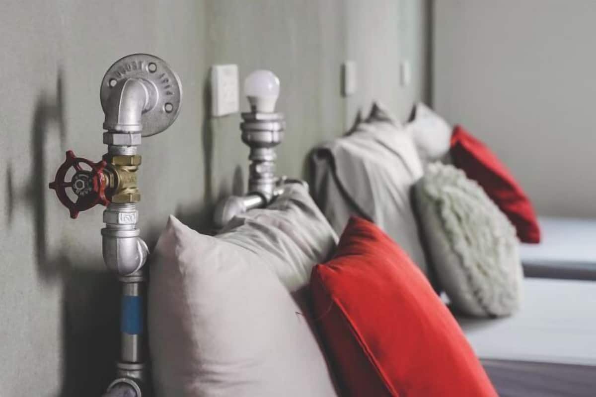 A wall-mounted pipe with a valve, a white pillow, and a red pillow against a wall.