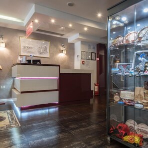 A reception desk with a modern design, a glass display case with souvenirs, and a framed picture on the wall. - Sultan Modern Hotel (Skopje)