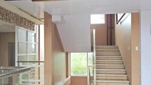 Ein geräumiger Innenraum mit einer Treppe zu einer oberen Etage, einem Glasgeländer und Blick ins Grüne.