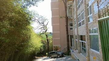A narrow street with a parked car, a building with a stone facade, and a tree-lined path.