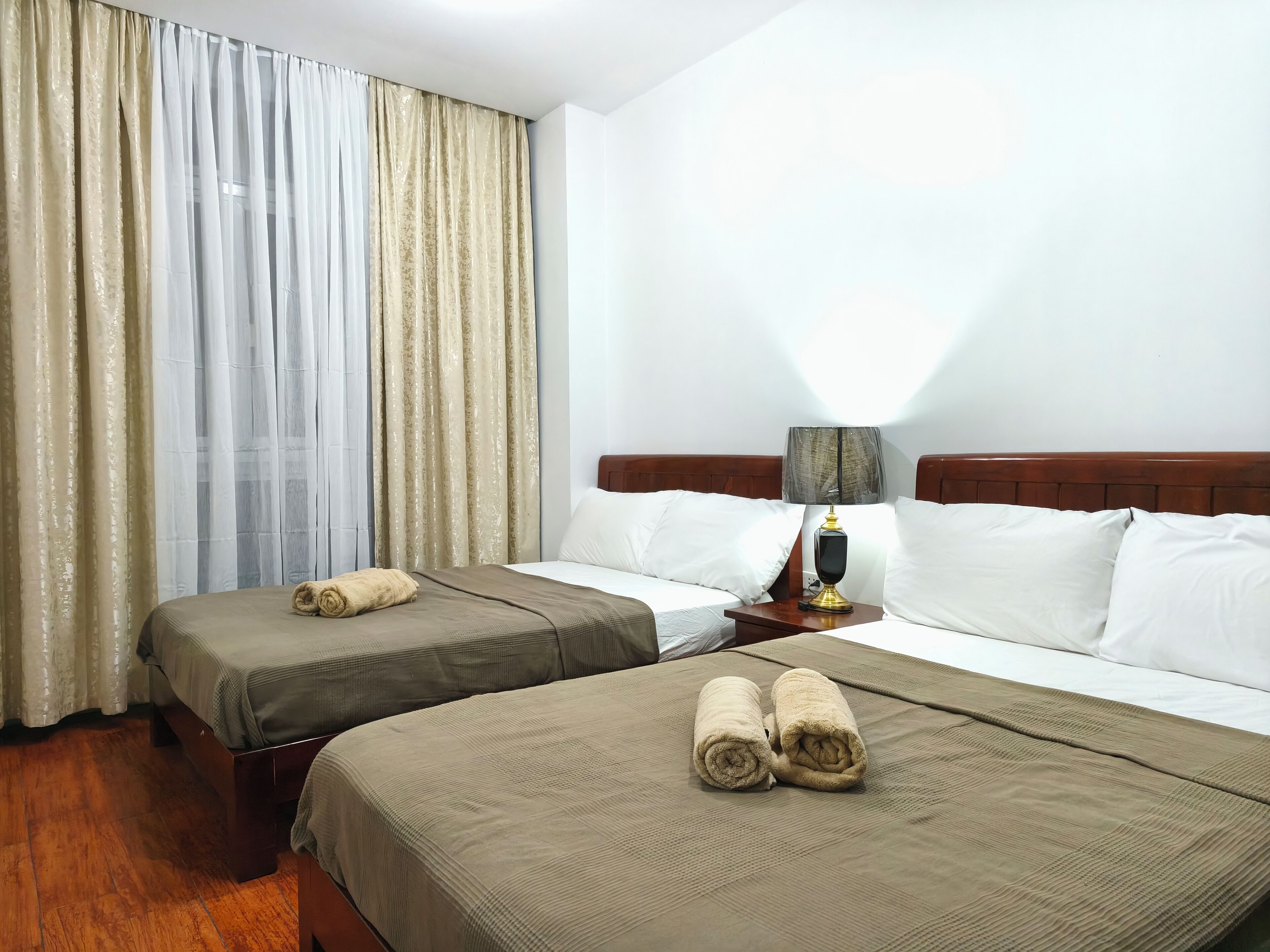 A hotel room with two beds, a nightstand with a lamp, and a window with curtains.