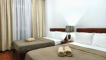 A hotel room with two beds, a nightstand with a lamp, and a window with curtains.