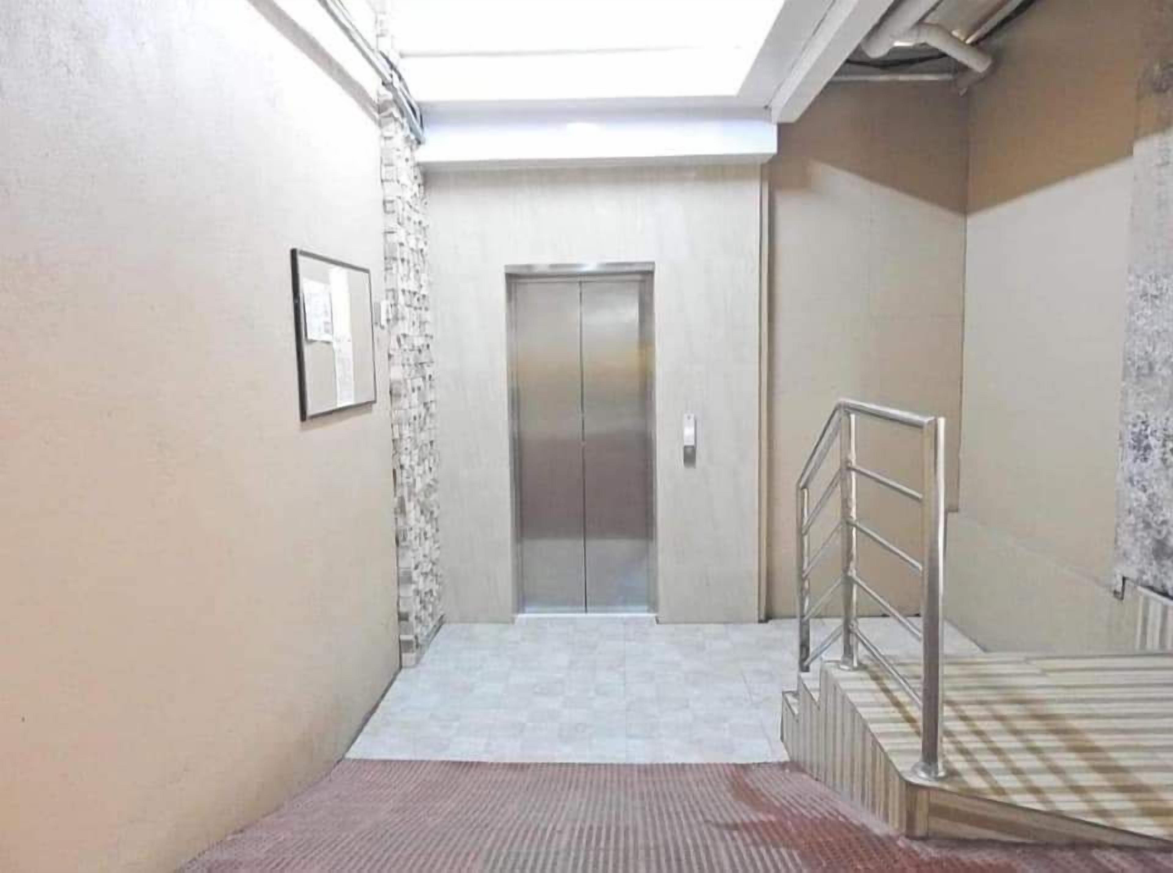 A narrow hallway with a tiled floor, a metal handrail, and a door at the end.