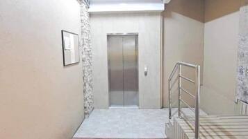 A narrow hallway with a tiled floor, a metal handrail, and a door at the end.
