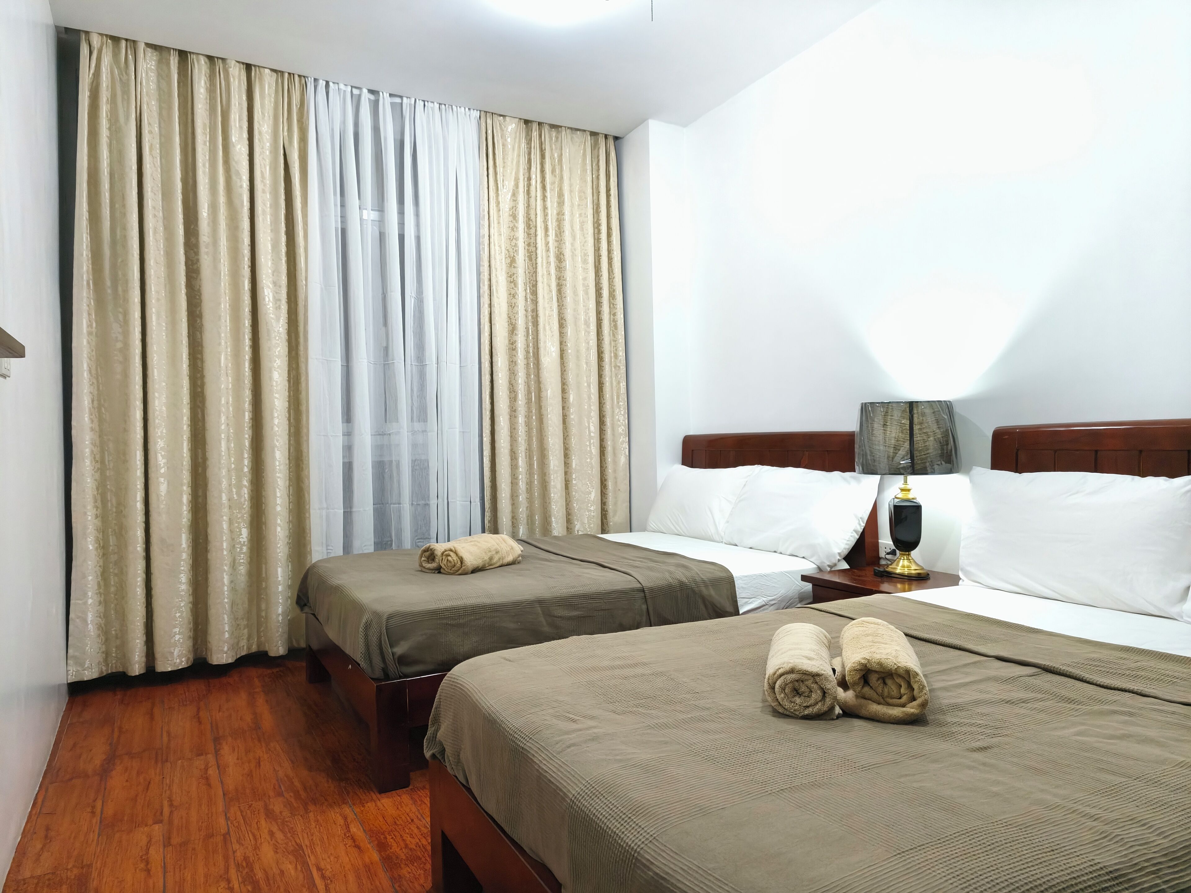 Une chambre d’hôtel avec deux lits, une table de chevet, une lampe et une fenêtre avec des rideaux.