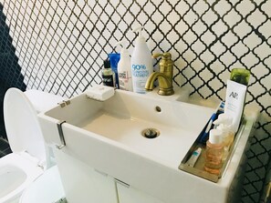 A bathroom with a white sink, a gold faucet, and toiletries including a protein treatment shampoo, a toothbrush, and a tube of toothpaste. - Avocado Guesthouse - Hostel (Seoul)