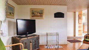 Una sala de estar con un televisor sobre una maleta antigua, un estante metálico y un cuadro en la pared.