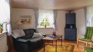 Una sala de estar acogedora con un sofá de cuero, una mesa de madera, un sillón verde, un aparador azul y una ventana con cortinas de encaje.