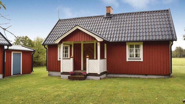 Una casa de madera roja con tejado de tejas grises, un porche y un pequeño jardín.