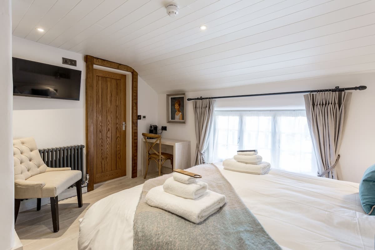 A hotel room with a bed, a chair, a desk, and a window with curtains.