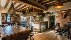A rustic bar area with wooden beams, a bar counter, stools, and a brick wall with a mounted animal head. - The Cow Dalbury (Ashbourne)