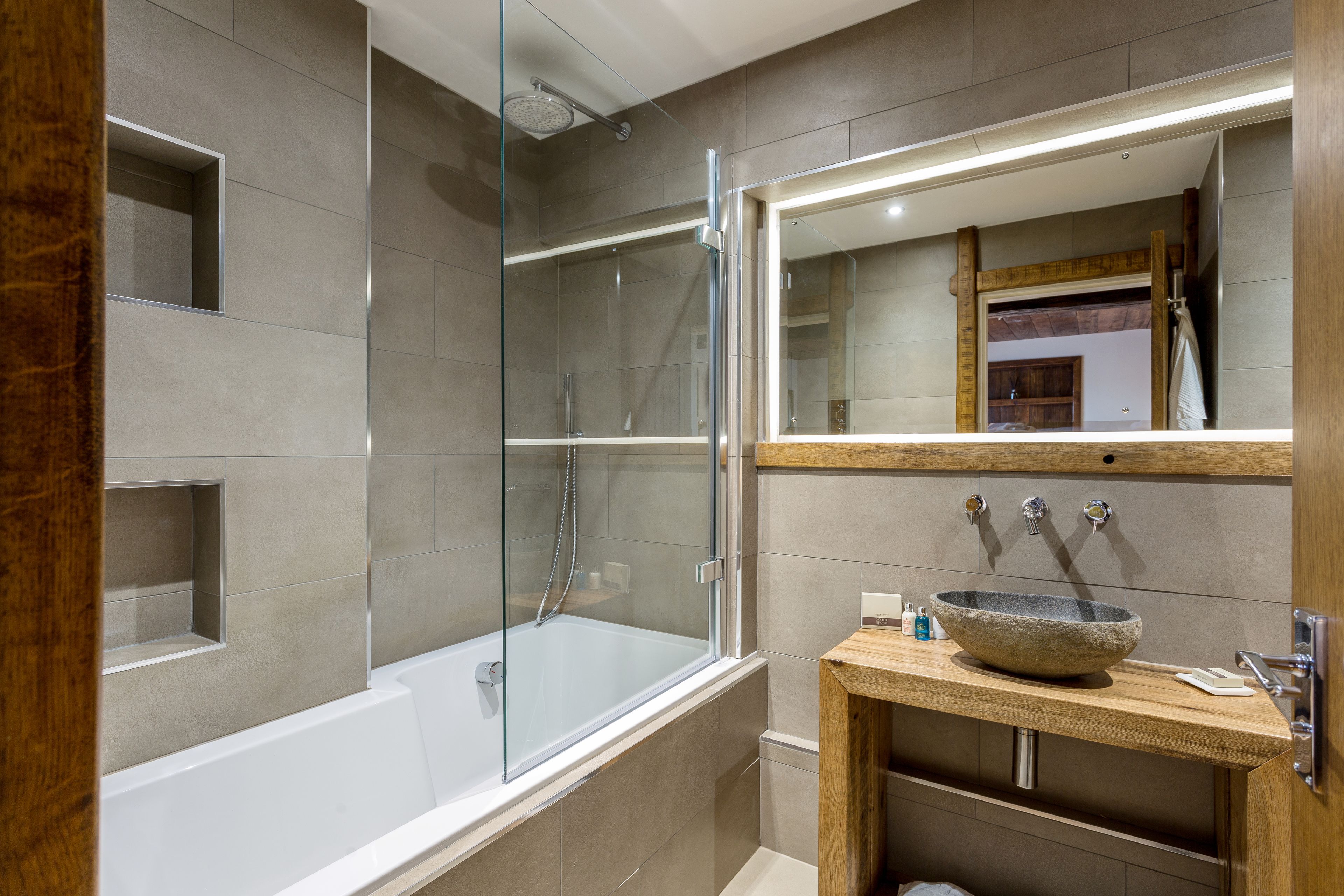 A modern bathroom with a glass-enclosed shower, a freestanding bathtub, and a wooden vanity with a stone basin.