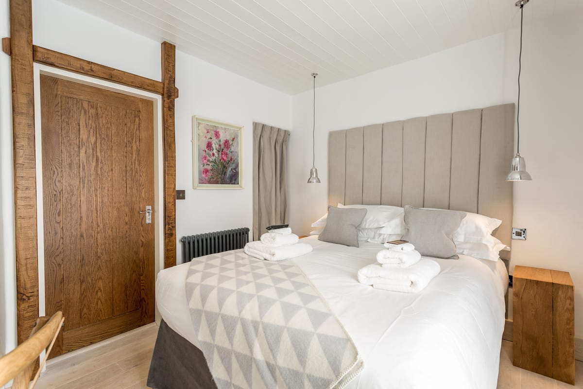 A bedroom with a large bed, wooden headboard, two bedside tables, a nightstand, a radiator, and a wooden door.