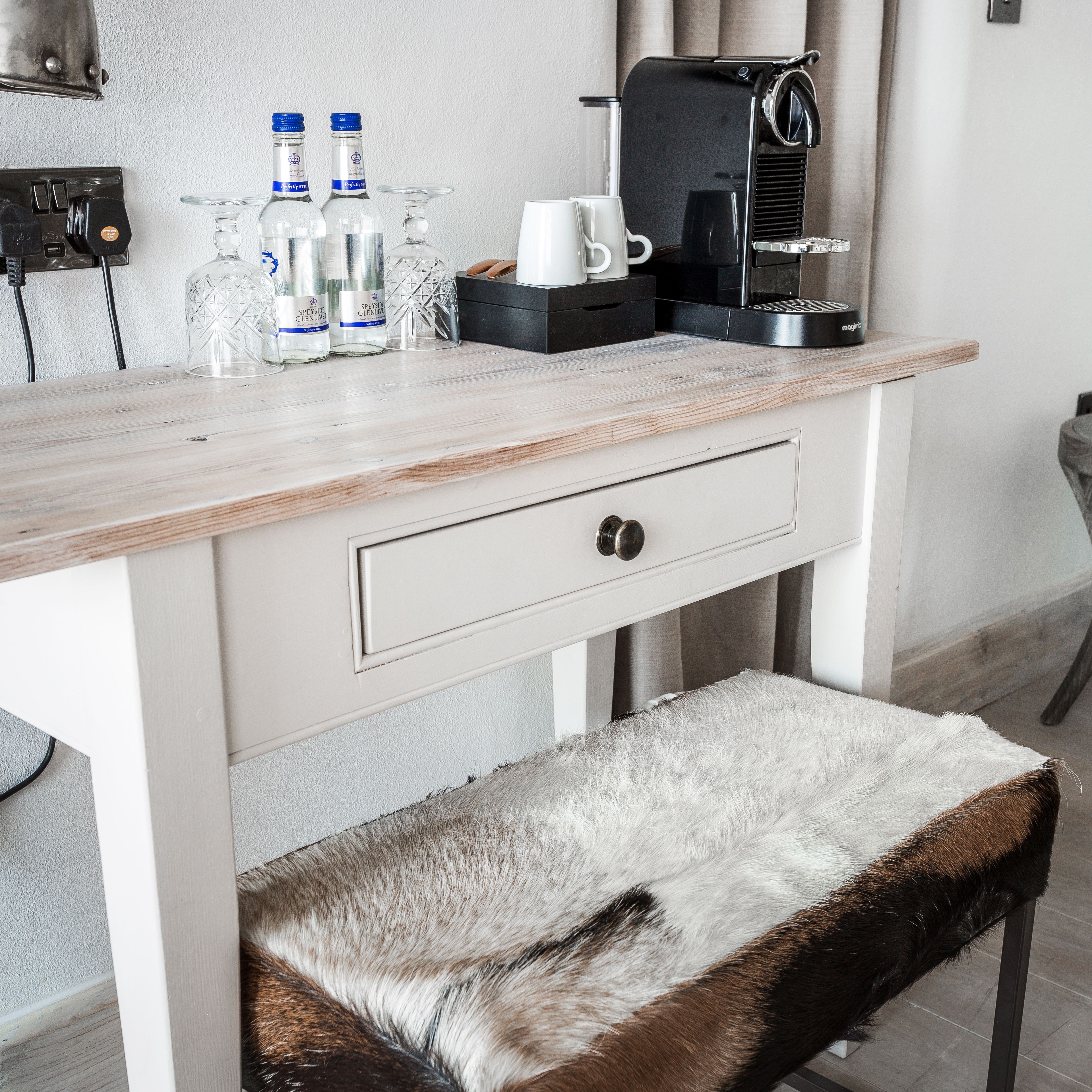 A modern kitchen with a wooden countertop, a coffee machine, and a bench with a fur throw.