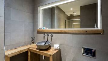 A modern bathroom with a stone sink, wooden vanity, and a large mirror with integrated lighting.