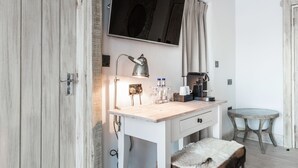 A room with a wooden ceiling, a white desk with a lamp, a bench, a television, and a small table. - The Cow Dalbury (Ashbourne)