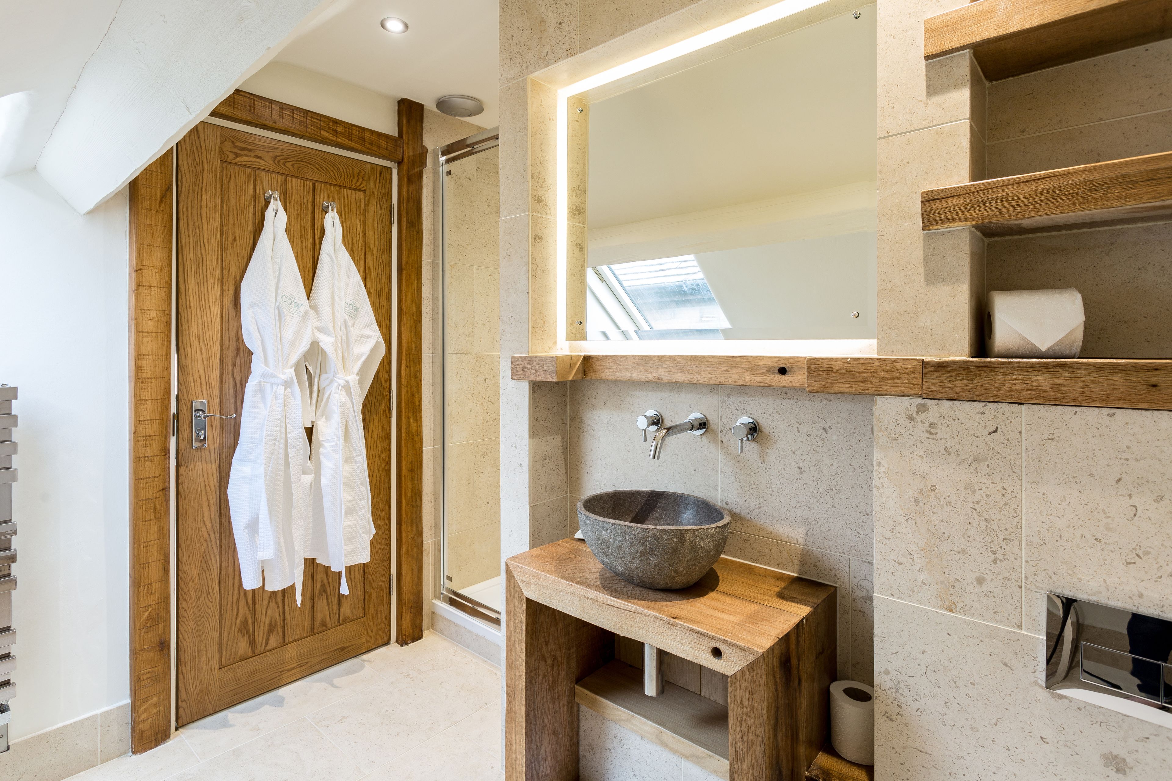 A modern bathroom with a wooden door, a large mirror, a stone sink, and a towel rack.