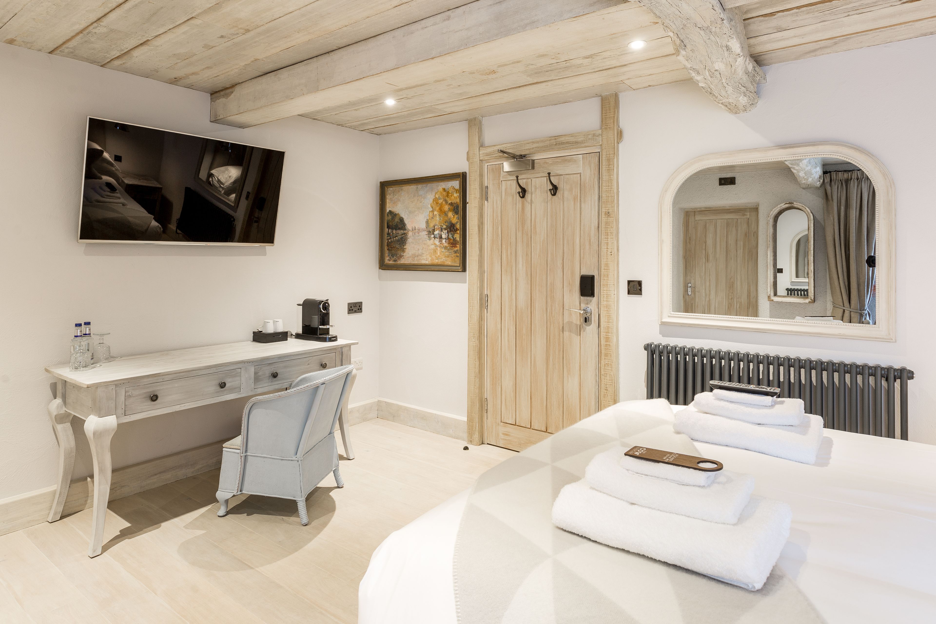 A bedroom with a bed, a desk, a chair, a painting, a wardrobe, and a mirror.