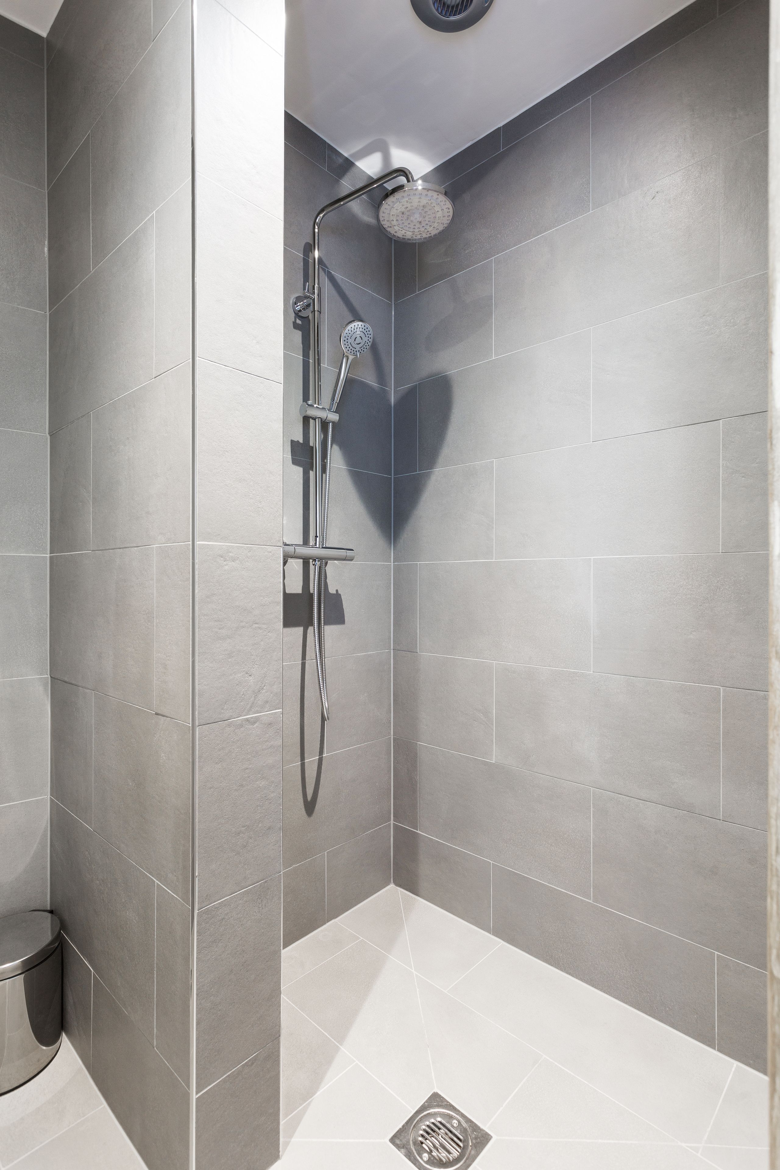 A modern shower with a handheld showerhead and a wall-mounted control panel.