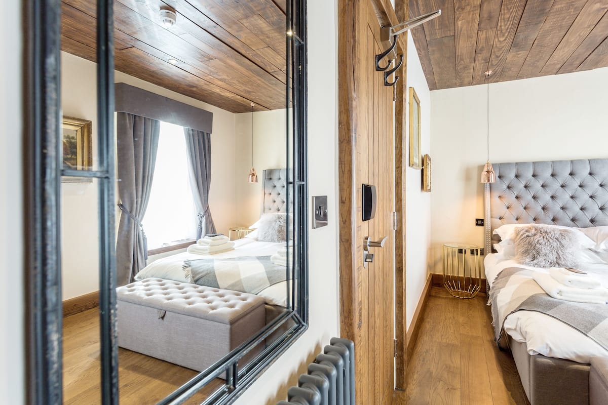 A bedroom with a large mirror, a tufted headboard, a wooden floor, and a radiator.