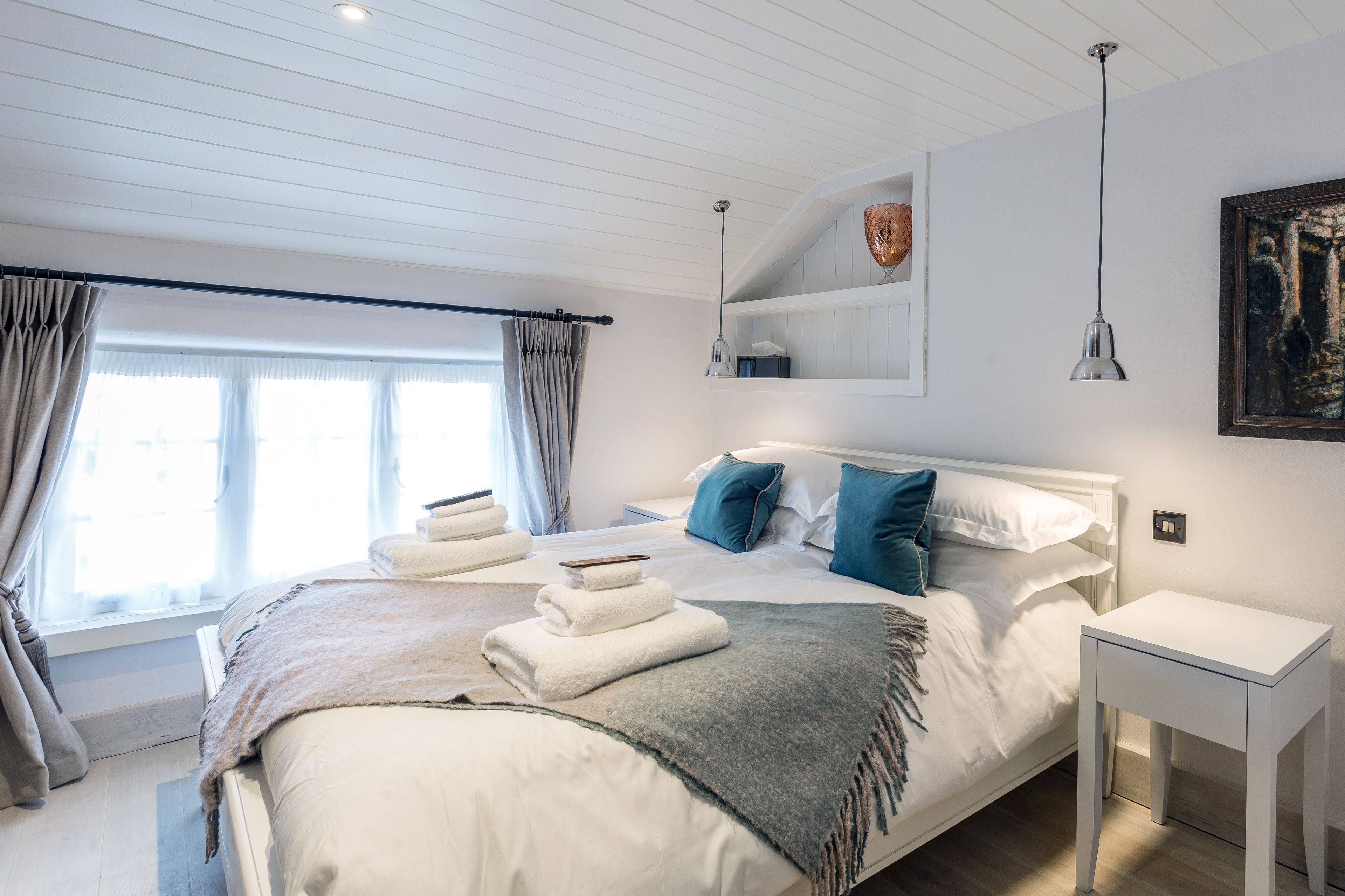 Une chambre à coucher moderne avec un grand lit, une table de chevet, une fenêtre avec des rideaux et un tableau au mur.