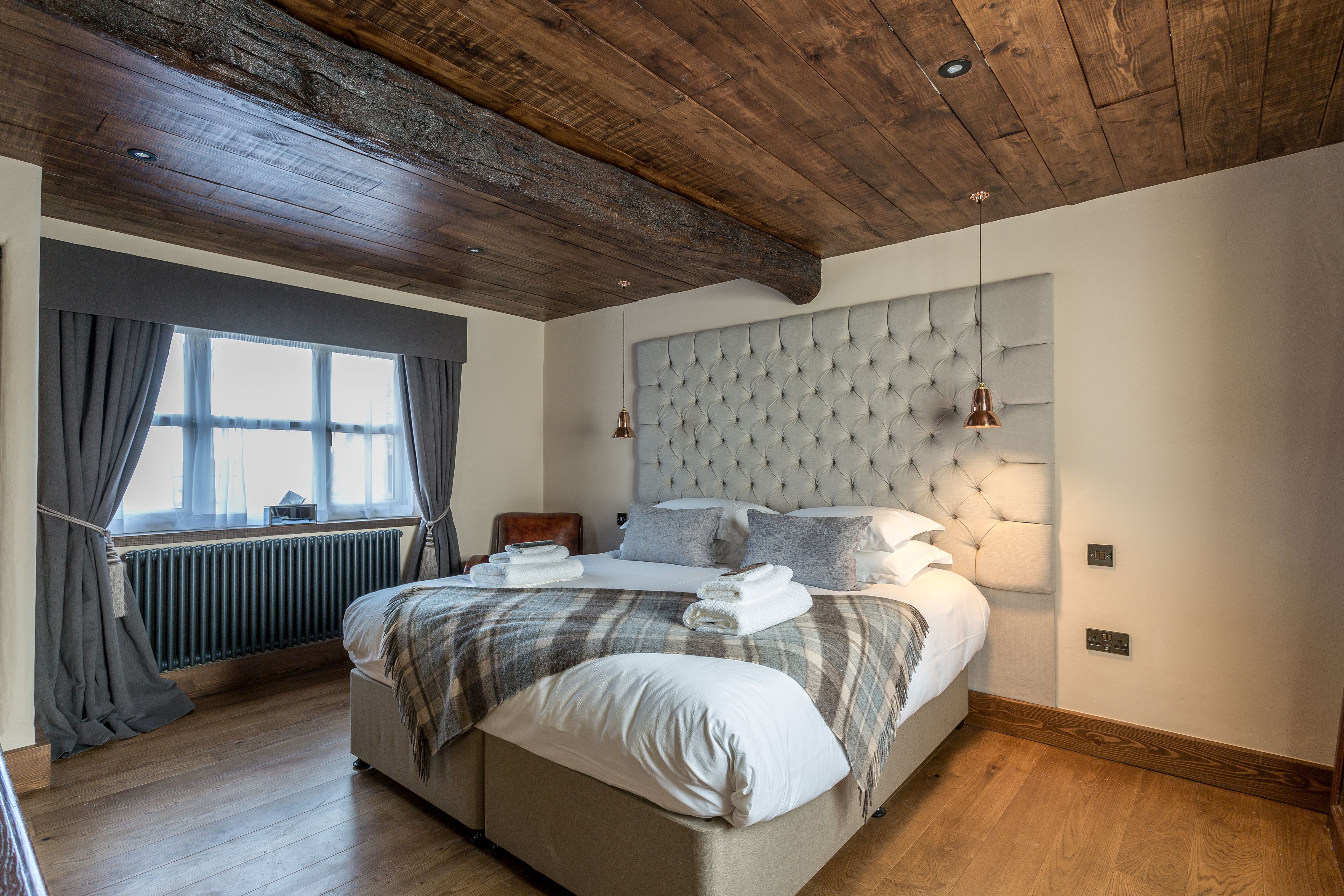 Un dormitorio con una cama grande, techo de madera, ventana con cortinas y un radiador.