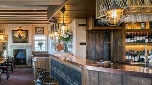 A bar area with wooden shelves, a fireplace, and a variety of bottles. - The Cow Dalbury (Ashbourne)
