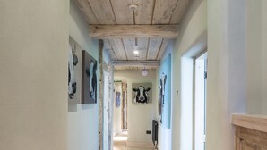 A hallway with wooden ceiling beams, light-colored walls, and artwork on the walls. - The Cow Dalbury (Ashbourne)