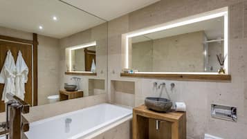 A modern bathroom with a large bathtub, wooden vanity, and a large mirror with integrated lighting.