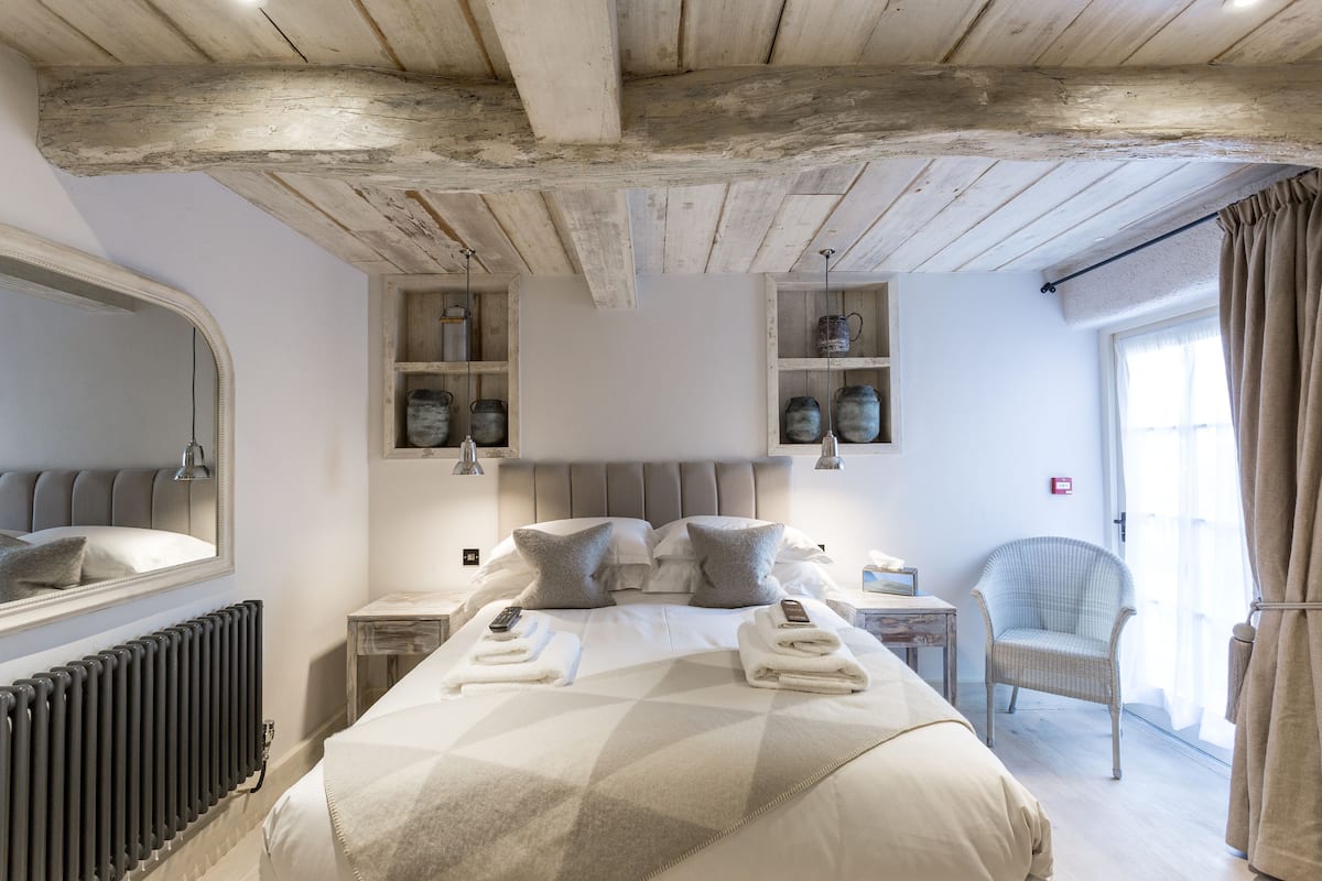 A bedroom with a large bed, a chest of drawers, a chair, and a window with curtains.