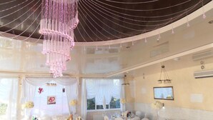 Une salle de réception pour mariage décorée de rideaux blancs, de tables rondes recouvertes de nappes blanches et de chaises habillées de housses blanches.
